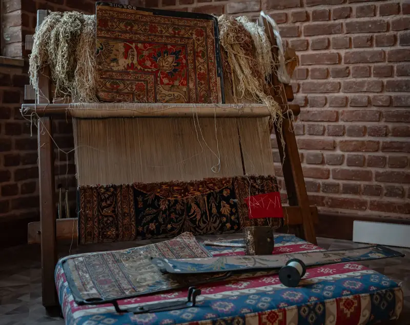 Ahşap el tezgâhında yarısı dokunmuş halı, yün çileleri ve önünde kilimler