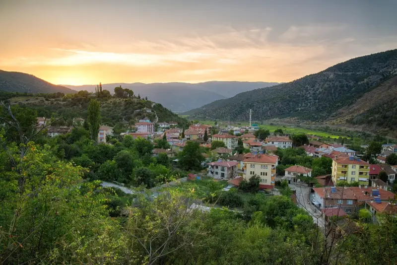 Gün batımında vadideki köy evleri, ağaçlar ve dağ silüetleri