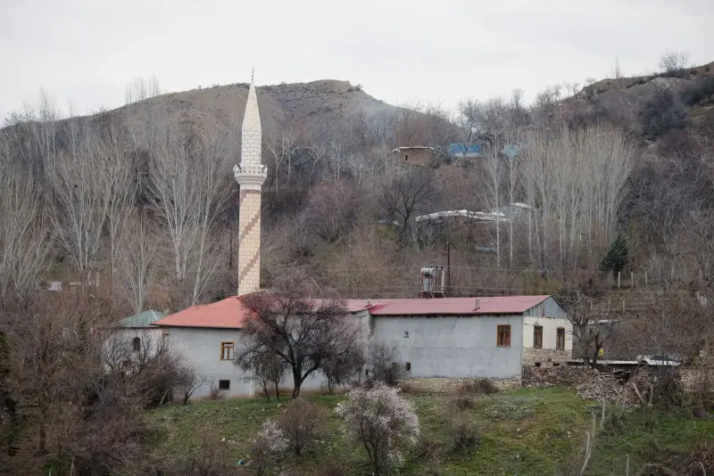 Tepe eteğinde, kavaklar ve çiçek açmış ağaçlar arasında minareli küçük köy camisi