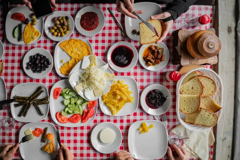 Kırmızı kareli örtü üzerinde peynir, zeytin, reçel, yumurta, sarma ve ekmekle zengin kahvaltı sofrası